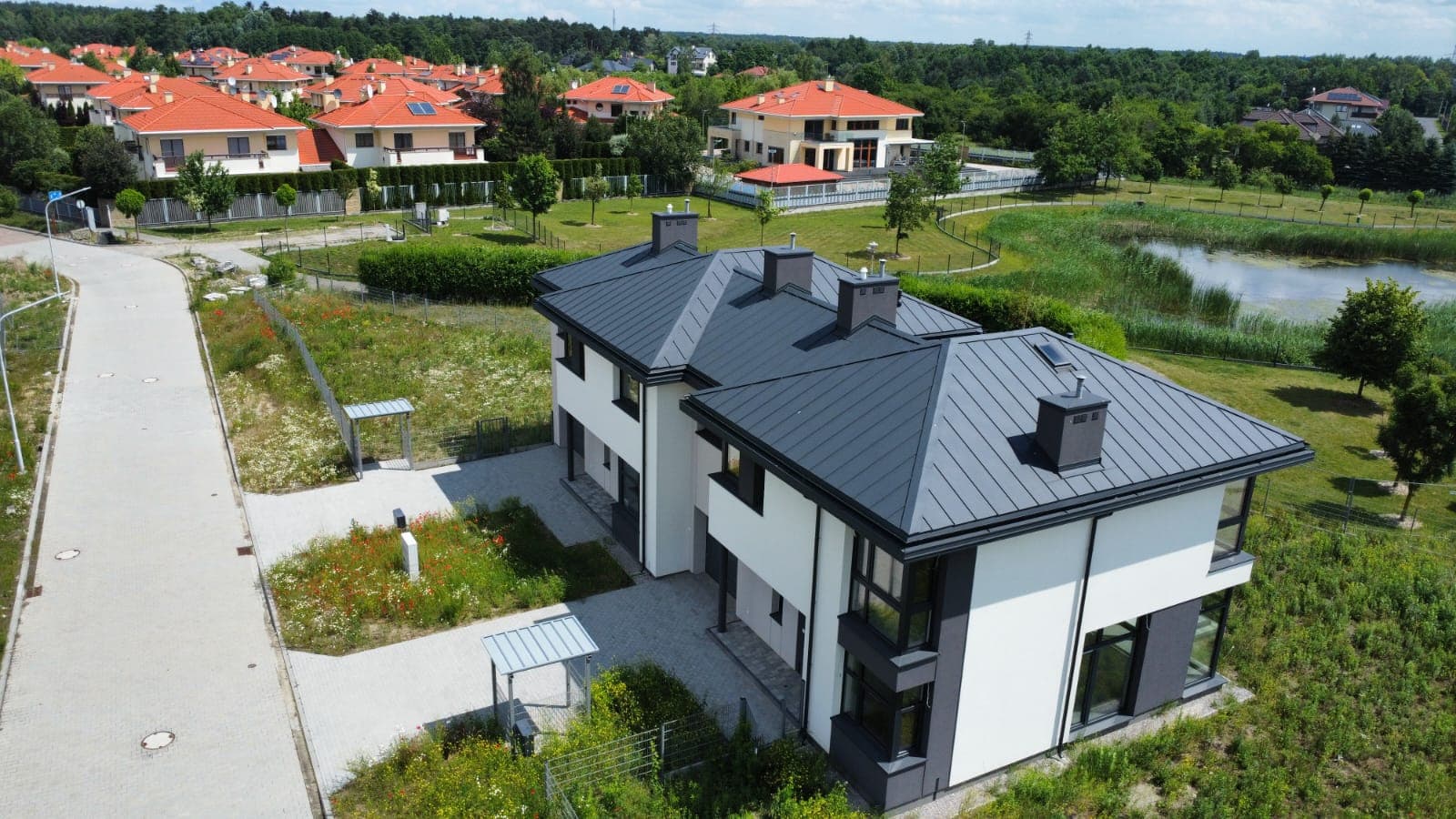 Dom z dachem z blachy na rąbek nad stawem — widok z drona